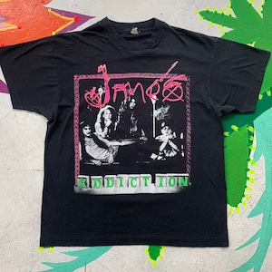May include: Black t-shirt featuring a pink and white graphic of the band "James" and the word "Addiction" in green block letters.