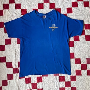 Op de afbeelding: Een koninklijk blauw t-shirt met een afbeelding van een brein en de tekst "brainwashed" in geel.