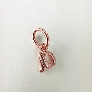 May include: Rose gold charm in the shape of the lowercase letter "p". The charm has a loop at the top for attaching to a bracelet or necklace. The letter is in a cursive font.