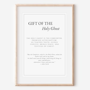 May include: A framed print featuring the words "GIFT OF THE Holy Ghost" in a minimalist style. The print contains a quote from John 14:26, with black text on a white background. The frame is a light wood colour.