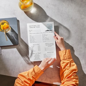 May include: A person holding a white "Getting to Know You" questionnaire with fill-in-the-blank sections. The questionnaire includes prompts for favorite things, yes or no questions, and "this or that" choices. A glass of orange-infused water sits nearby.