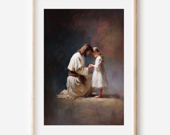 May include: A framed print depicts a kneeling figure in white robes, holding the hands of a young girl in a white dress. The artwork has a soft, painterly style with warm, earthy tones and a focus on the figures' interaction. The frame is a light wood color.