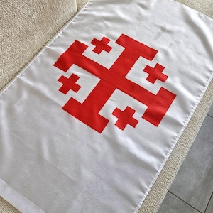 Könnte beinhalten: Weißes rechteckiges Banner mit einem großen roten Jerusalemer Kreuz-Design. Die Flagge besteht aus einem glatten Material, möglicherweise Satin. Das Jerusalemer Kreuz ist ein großes Kreuz mit vier kleineren Kreuzen in jedem Quadranten.