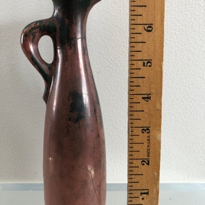 Könnte beinhalten: Ein kleiner, brauner und grüner Keramik Krug mit Henkel. Der Krug hat eine craquelée Glasur und einen grünen Rand.