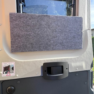 Könnte beinhalten: Eine graue Filzplatte, die in einer Fahrzeugtür installiert ist und sich unter einem Fenster befindet. Die Tür ist hellbeige mit einem schwarzen Griff und einem dunkelgrauen unteren Bereich. Ein Aufkleber mit einem Warnsymbol ist sichtbar.