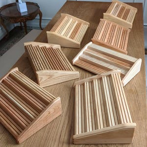 May include: Several wooden desk organizers are arranged on a wooden table. Each organizer has a slatted design with a stepped base. The wood tones vary from light to medium brown, showcasing the natural grain.