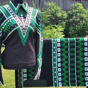 May include: Black equestrian show shirt with green and white geometric embellishments. The shirt is displayed with a matching black saddle pad featuring a green and white pattern. The shirt has long sleeves and a collared neckline.