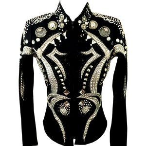 Puede incluir: Chaqueta de exhibición ecuestre negra con elaborados adornos de cristal plateado y transparente. La chaqueta presenta un cuello alto y una cremallera frontal. Los patrones decorativos adornan los hombros, el pecho y las mangas, creando un efecto deslumbrante.