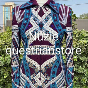 Könnte beinhalten: Eine violette Reitshowjacke mit aufwendiger Perlenarbeit und Verzierungen. Die Jacke hat einen Reißverschluss vorne, einen Kragen und ist mit weißen, türkisfarbenen und silbernen Akzenten verziert. Der Text "Nuzie questrianstore" ist auf der Vorderseite zu sehen.