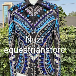 Könnte beinhalten: Schwarze Reitjacke mit aufwendigen blauen und silbernen Verzierungen. Die Jacke hat einen Reißverschluss, einen Kragen und lange Ärmel. Das Design umfasst geometrische Muster und den Text "Nuzi equestrianstore".