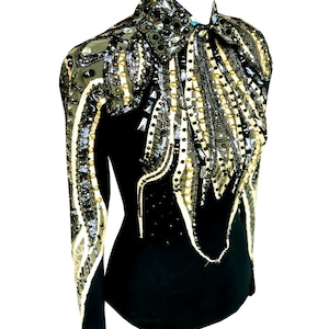 Könnte beinhalten: Schwarzes, langärmliges Reit-Show-Shirt mit aufwendigen Verzierungen. Der Oberkörper und die Ärmel weisen komplizierte Muster aus silbernen, goldenen und klaren Pailletten, Perlen und Kristallen auf. Der Kragen ist hoch.