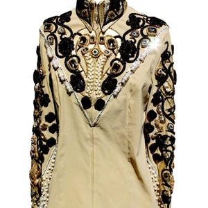 May include: Tan equestrian show jacket with black floral and geometric embellishments. The jacket features gold and silver accents, rhinestones, and pearl-like beads. The collar and sleeves are intricately detailed with decorative elements.