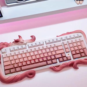 May include: A white and pink mechanical keyboard with a gradient keycap design. The keyboard is accented with a pink fox-like sculpture that wraps around the edges. The keys are a gradient of pink hues.