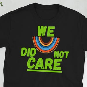 Peut inclure: T-shirt noir avec l'inscription verte « WE DID NOT CARE » et un motif arc-en-ciel. L'arc-en-ciel présente des rayures bleues, orange et marron. Un t-shirt décontracté pour tous les jours.