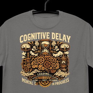 May include: A grey t-shirt with a graphic design. The design includes the text "COGNITIVE DELAY" and "MENTAL IN PROGRESS", an hourglass, gears, and a brain. The word "LOADING..." is in the center of the design.