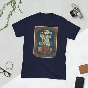 Peut inclure: T-shirt bleu marine avec un motif de style vintage indiquant "I'M MY FAMILY'S UNPAID TECH SUPPORT". Le motif comprend une illustration de radio rétro. Le t-shirt est en tissu doux.