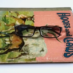 May include: A vintage children's book titled "Hoofs and Claws" with a pair of brown eyeglasses resting on top. The book cover features a colorful illustration of two goats.