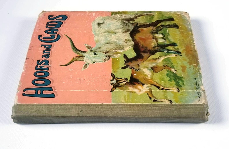 May include: A vintage children's book titled "Hoofs and Claws" with a pink cover featuring an illustration of a white goat with horns and two brown goats. The book has a green cloth spine.