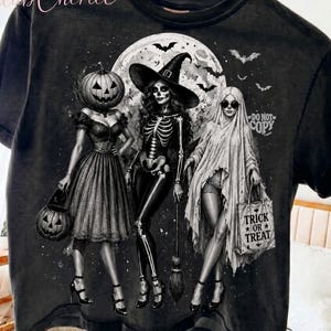 Könnte beinhalten: Ein schwarzes T-Shirt im Vintage-Wasch-Look mit einer Grafik von drei Figuren: eine Person mit Kürbiskopf, eine Skelett-Hexe und eine geisterhafte Gestalt. Das Design zeigt einen Vollmond, Fledermäuse und eine Tasche mit dem Text "TRICK OR TREAT" und "DO NOT COPY".