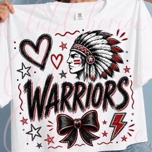 Puede incluir: Una camiseta blanca de manga corta con un estampado gráfico de una persona con un tocado de plumas, la palabra WARRIORS en letras negras negritas, un lazo negro, corazones, estrellas y un rayo en tonos rojos y negros.