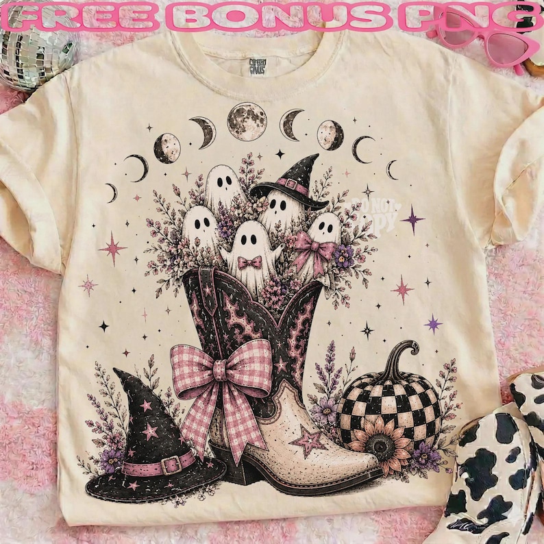 May include: A cream-colored t-shirt featuring a graphic of a cowboy boot filled with ghosts, a witch hat, and flowers. The design includes a checkered pumpkin, a moon phase cycle, and stars. A large pink plaid bow is attached to the boot.