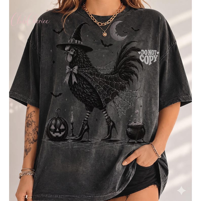 May include: A charcoal gray oversized t-shirt featuring a graphic of a chicken wearing a witch hat, a spiderweb cape, and striped stockings with high-heeled boots. The design includes a jack-o'-lantern, a cauldron, and the text DO NOT COPY.