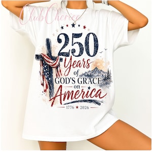 K&ouml;nnte beinhalten: Ein wei&szlig;es T-Shirt mit einem grafischen Design, das ein Kreuz mit einer amerikanischen Flagge, eine Berglandschaft und den Text 250 Years of GOD'S GRACE on America 1776-2026 zeigt. Das Design enth&auml;lt rote, wei&szlig;e und blaue Farben sowie Sterne.