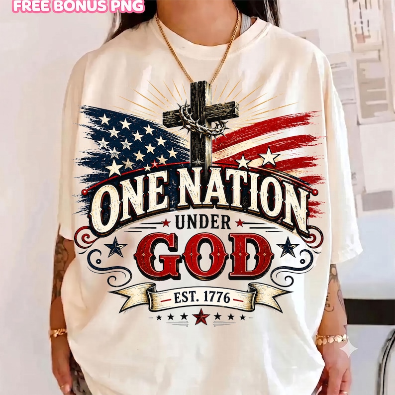 K&ouml;nnte beinhalten: Ein cremefarbenes T-Shirt mit einer Grafik eines Holzkreuzes mit Dornenkrone vor einer verwaschenen amerikanischen Flagge. Der Text ONE NATION UNDER GOD EST. 1776 ist in fetten, stilisierten Buchstaben in Rot, Wei&szlig; und Blau abgebildet.