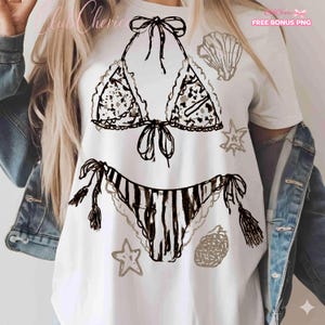 Puede incluir: Camiseta blanca con un dise&ntilde;o de bikini dibujado a mano en negro y gris, acompa&ntilde;ada de ilustraciones de conchas marinas y estrellas de mar. La camiseta tiene los textos "Club Cherice" y "FREE BONUS PNG".