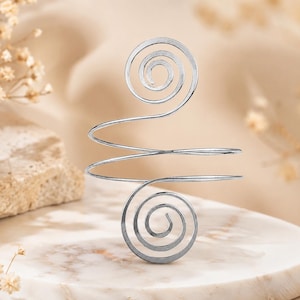 May include: A silver-toned metal ring featuring a continuous wire design that forms two distinct spirals at the top and bottom, connected by a central horizontal band. The wire is smooth and polished, creating a symmetrical, open-ended structure.