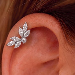 May include: A silver-toned ear cartilage piercing featuring a cluster of five marquise-cut clear stones arranged in a leaf-like pattern, accented by a single small round clear stone at the base, secured against the upper edge of the ear cartilage.