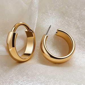 Peut inclure: Une paire de boucles d'oreilles créoles dorées. Une boucle est fermée, l'autre est ouverte, montrant la tige. Les boucles d'oreilles ont une finition lisse et polie et une forme arrondie. Les bijoux sont présentés sur une surface blanche texturée.