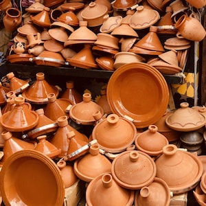 Peut inclure: Un assortiment de tagines et de plats de service en terre cuite. Les tagines ont des couvercles coniques et des bases arrondies, tandis que les plats sont plats et circulaires. Les articles sont de couleur orange terreux, empilés.