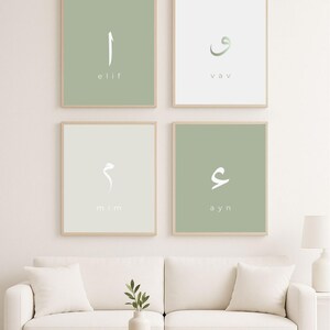 Op de afbeelding: Vier ingelijste kunstprints met Arabische kalligrafie. Elke print toont een andere letter in wit tegen een gedempte groene of gebroken witte achtergrond. De frames zijn licht van kleur en de prints worden boven een witte bank weergegeven.