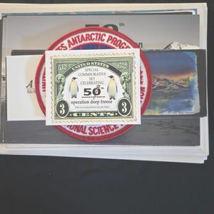 Könnte beinhalten: Eine Sammlung von Artikeln zum US-amerikanischen Antarktis-Programm. Enthält eine Gedenkbriefmarke zum 50. Jahrestag der Operation Deep Freeze, einen Aufnäher und andere Drucksachen. Die Briefmarke zeigt zwei Pinguine und hat einen Wert von 3 Cent.