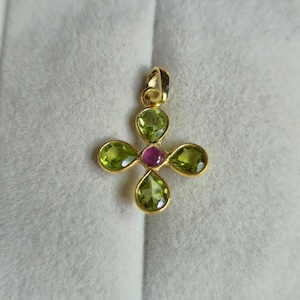 May include: A gold pendant featuring a four-petaled flower design. Each petal is set with a pear-shaped, faceted light green peridot gemstone. A single, round, faceted magenta-colored gemstone is set in the center of the flower arrangement.