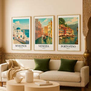Puede incluir: Tres láminas enmarcadas de arte de viaje con vistas de Mykonos, Venecia y Portofino. Cada lámina tiene un marco dorado y el nombre de la ciudad en texto blanco. La lámina de Mykonos muestra un edificio blanco con una cúpula azul. La lámina de Venecia muestra un canal. La lámina de Portofino muestra edificios coloridos.