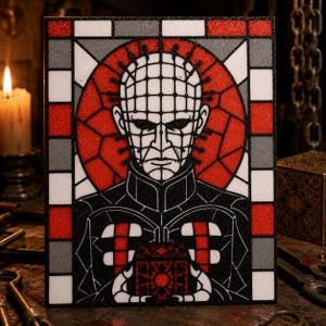 May include: A rectangular wall art piece featuring a stained glass style illustration of a pale, grid-patterned humanoid figure with pins in their head, wearing a black outfit and holding a small, ornate, dark red and black puzzle box.