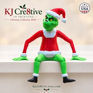 May include: A 3D printed green character figure wearing a red shirt and Santa hat with white trim, sitting with arms outstretched. Text includes KJ Cre8tive 3D Printing Christmas Collection 2026, Made in the USA, and kjcre8tive.etsy.com.