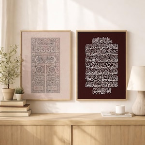 Puede incluir: Dos impresiones artísticas enmarcadas con caligrafía árabe. Una impresión tiene un fondo rosa claro con patrones negros ornamentados. La otra impresión tiene un fondo rojo oscuro con caligrafía blanca. Ambas están en marcos de madera marrón claro, exhibidas en un mueble de madera.