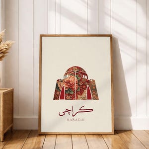 Pode incluir: Uma impressão de arte emoldurada com uma ilustração estilizada de um edifício com uma cúpula com padrão floral. A impressão inclui a palavra "Karachi" em urdu e inglês, em um fundo creme.