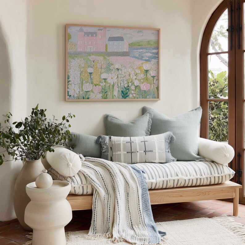 May include: A cozy living space featuring a wooden daybed with striped cushions and a fringed throw blanket. Decorative pillows in shades of blue and white add to the comfort. A framed landscape painting hangs above the daybed, and a vase with greenery sits nearby.