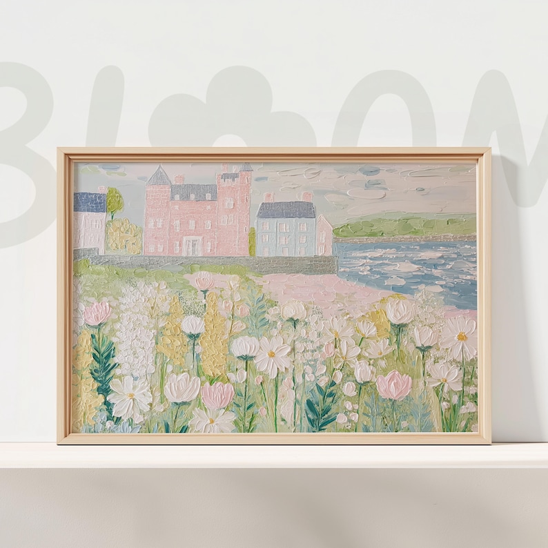 May include: A framed landscape painting featuring a coastal scene with a pink castle, blue houses, and a field of white and pink flowers. The artwork is set against a backdrop of a blue sea and sky, with a light wooden frame.