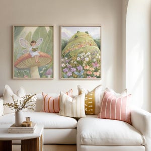 May include: Two framed watercolor art prints. One depicts a fairy reading on a mushroom, the other a flowered hill. The prints hang above a white sofa with decorative pillows in pink, white, and yellow.