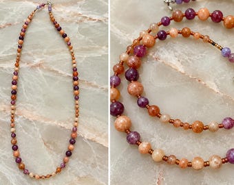 May include: A beaded necklace featuring alternating round peach-colored and deep purple beads of varying sizes, accented with small metallic copper-toned spacer beads and finished with a silver-toned circular clasp closure.