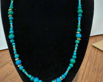 May include: A long necklace featuring a strand of round turquoise and teal beads in varying sizes, interspersed with small, metallic gold-toned spacer beads. The beads are arranged in a repeating pattern along the entire length of the necklace.