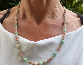 May include: A beaded necklace featuring alternating round beads in soft shades of peach and pale mint green. The beads vary slightly in size and are strung together in a continuous pattern, creating a delicate and colorful accessory.