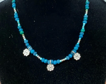 May include: A beaded necklace featuring a strand of small, faceted blue and turquoise beads interspersed with tiny silver-toned spacer beads. Three silver-toned metal charms shaped like six-petaled flowers hang from the necklace.