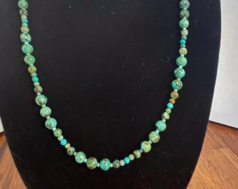 May include: A beaded necklace featuring a strand of round turquoise stones in varying shades of blue and green with dark brown matrix veining, interspersed with smaller, solid bright turquoise accent beads throughout the length.