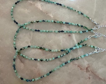May include: Three beaded necklaces featuring a mix of small, round, faceted green and dark blue beads. Each necklace is strung on a thin cord and finished with a silver-toned metal lobster claw clasp and a short extender chain at the ends.